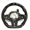 CJ Mod Garage BMW G-chassis LED carbon fiber steering wheel on white background featuring integrated RGB LED shift indicators, digital top display module, gloss carbon fiber shell, Alcantara side grips, flat-bottom racing profile, exposed OEM mounting structure, compatible with BMW G02 G05 G06 G09 G11 G12 G15 G20 G22 G28 G29 G30 G38 G80 G82 F40 F90