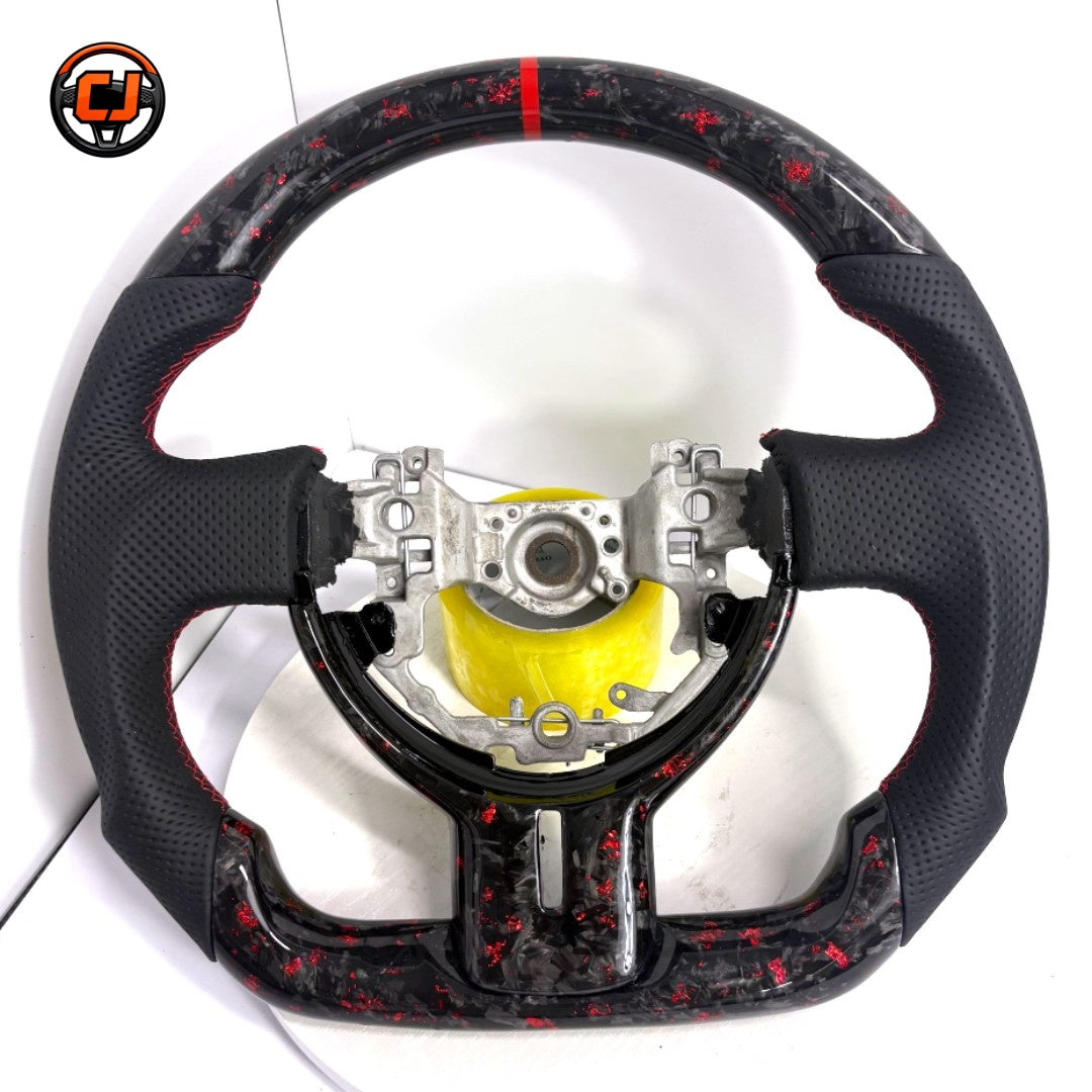 Forged carbon Toyota 86 performance steering wheel with red metallic flakes, perforated leather sections and ergonomic racing grip crafted by CJ Mod Garage