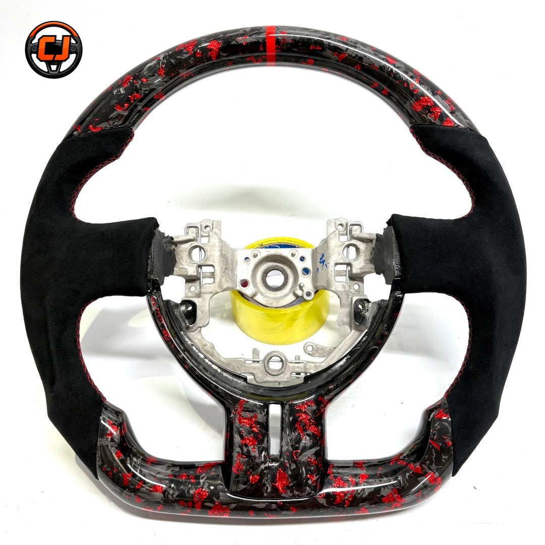 Toyota GT86 aftermarket steering wheel in forged carbon fiber with red metallic flakes, suede side grips, ergonomic contours and custom motorsport details by CJ Mod Garage