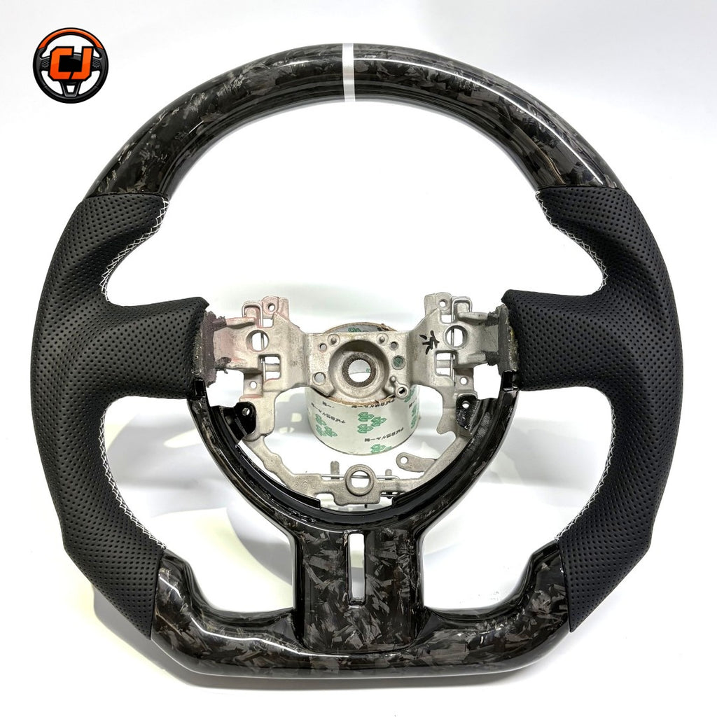 Custom Toyota GT86 steering wheel crafted from forged carbon fiber and premium perforated leather, showcasing white 12 o’clock stripe and ergonomic sport grip design by CJ Mod Garage