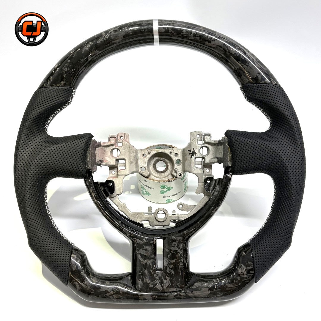 Custom Toyota GT86 steering wheel crafted from forged carbon fiber and premium perforated leather, showcasing white 12 o’clock stripe and ergonomic sport grip design by CJ Mod Garage