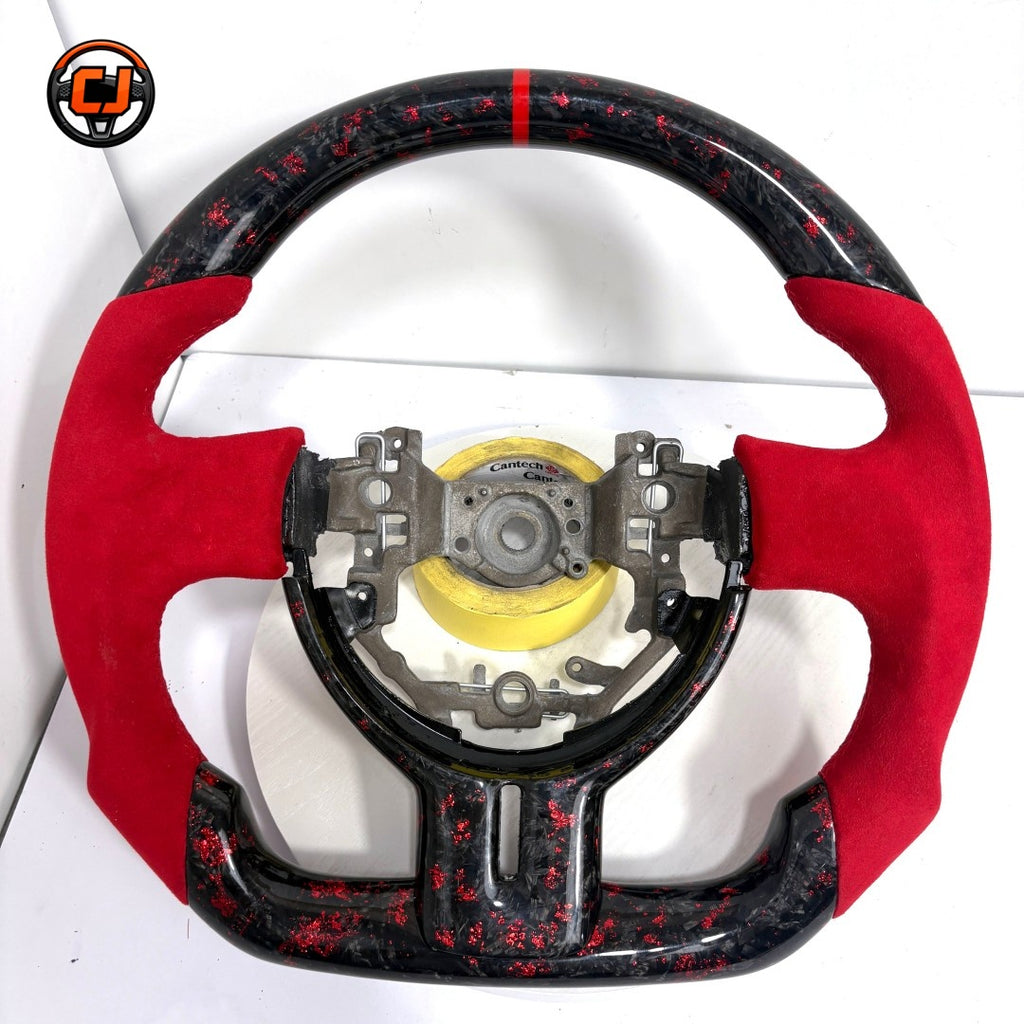 Toyota GT86 performance steering wheel crafted from forged carbon fiber with red metallic flakes, Alcantara grips and sport flat-bottom geometry by CJ Mod Garage
