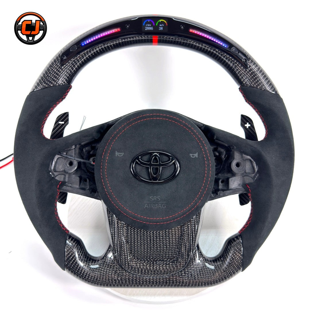 Custom Toyota GR Supra A90 A91 steering wheel crafted with premium carbon fiber, Alcantara wrapping, integrated LED shift lights, red center stripe and paddle shifters by CJ Mod Garage