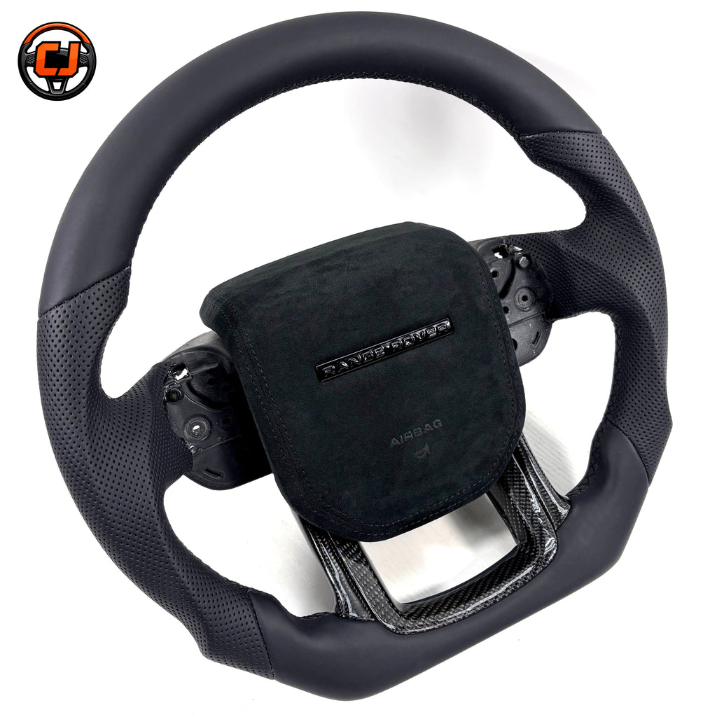 Studio product photo of custom Range Rover Evoque steering wheel with black perforated leather grips, Alcantara airbag cover and carbon fiber lower spoke trim