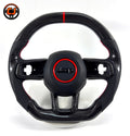 Studio product photo of custom Jeep Wrangler carbon fiber steering wheel with flat bottom design, black perforated leather grips, red stitching, red center stripe and Jeep airbag cover