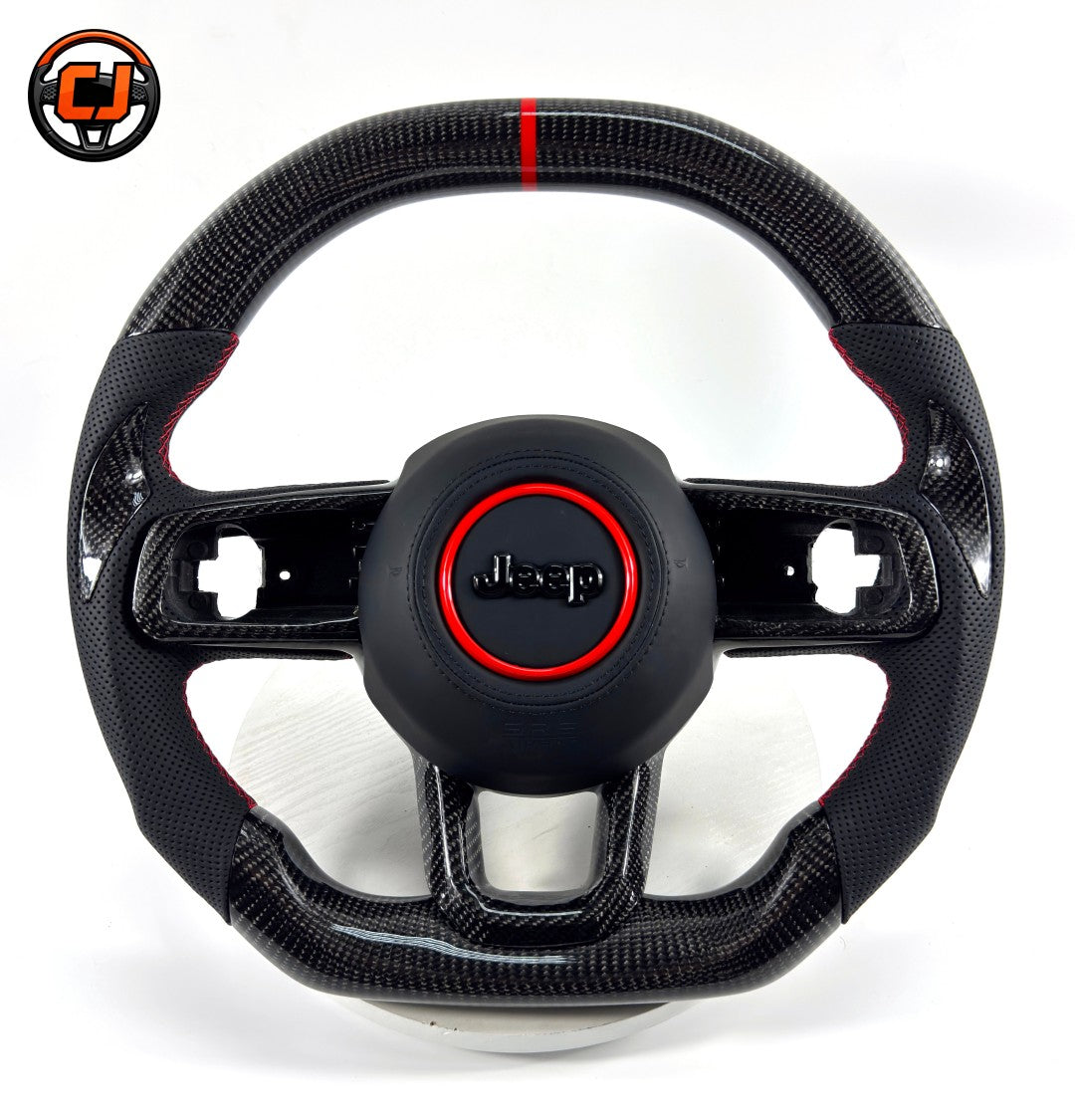 Studio product photo of custom Jeep Wrangler carbon fiber steering wheel with flat bottom design, black perforated leather grips, red stitching, red center stripe and Jeep airbag cover