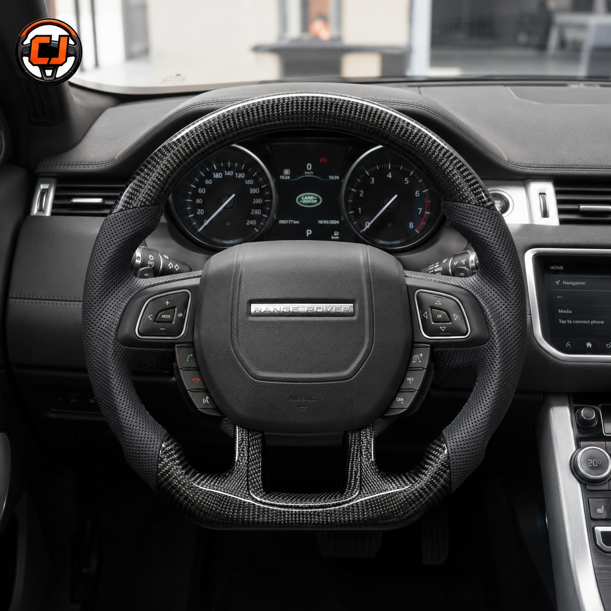 Front interior view of custom Range Rover Evoque steering wheel with carbon fiber upper rim, carbon fiber lower spoke, black perforated leather grips and original control buttons