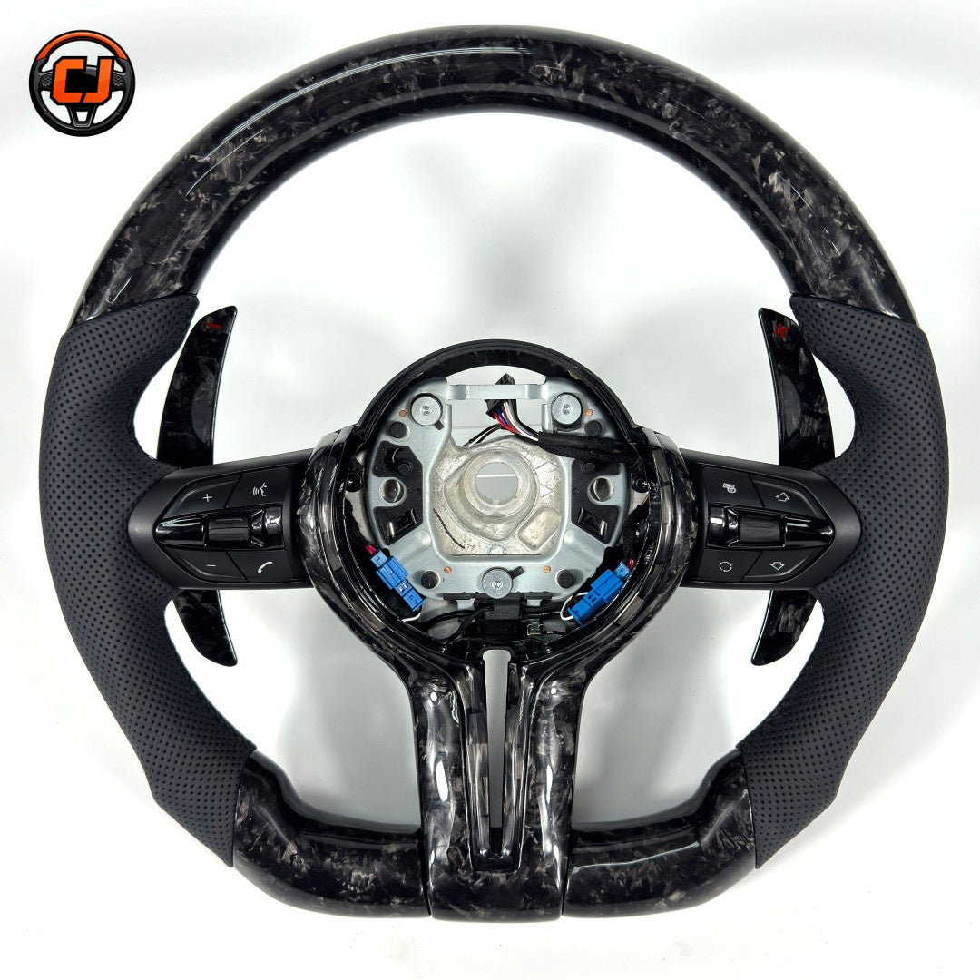 Black forged carbon fiber BMW steering wheel with perforated leather side grips, multifunction controls, paddle shifters, and exposed airbag mounting structure compatible with BMW F10 F11 F15 F18 F20 F23 F25 F30 F32 F35 F40 F80 E84 E87 E90 E92 E93