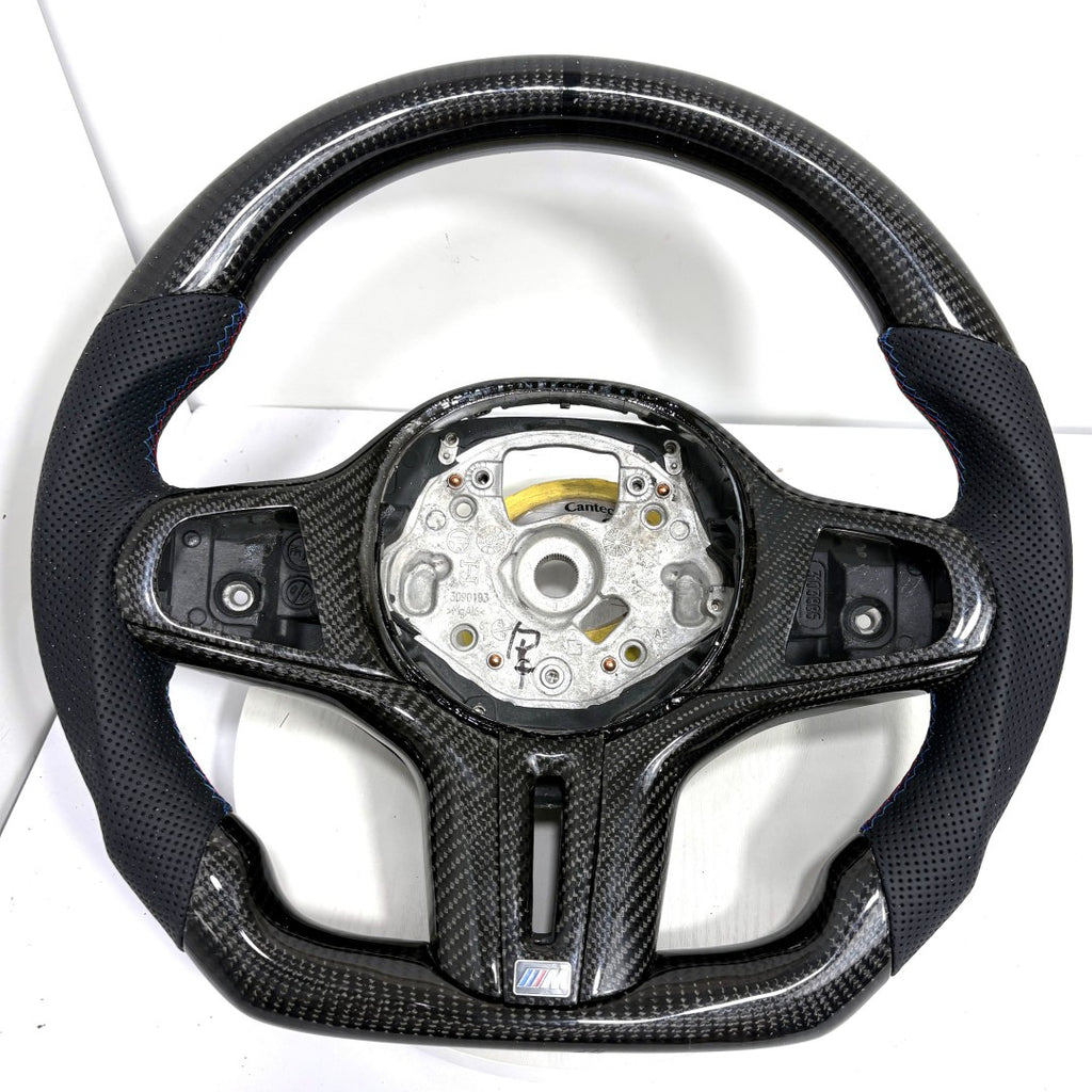BMW G-series carbon fiber steering wheel frame with round airbag mounting layout, perforated leather grips, and flat-bottom sport contour on white background for BMW G02 G05 G06 G09 G11 G12 G15 G20 G22 G28 G29 G30 G38 G80 G82 F40 F90