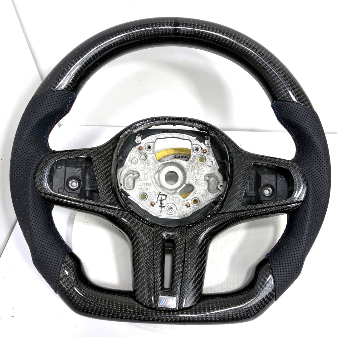 BMW G-series carbon fiber steering wheel frame with round airbag mounting layout, perforated leather grips, and flat-bottom sport contour on white background for BMW G02 G05 G06 G09 G11 G12 G15 G20 G22 G28 G29 G30 G38 G80 G82 F40 F90