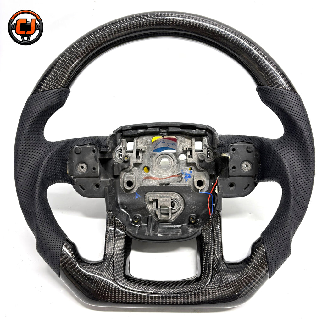 Studio product photo of custom Range Rover Evoque carbon fiber steering wheel with black perforated leather grips, flat bottom carbon fiber trim and exposed central mounting structure