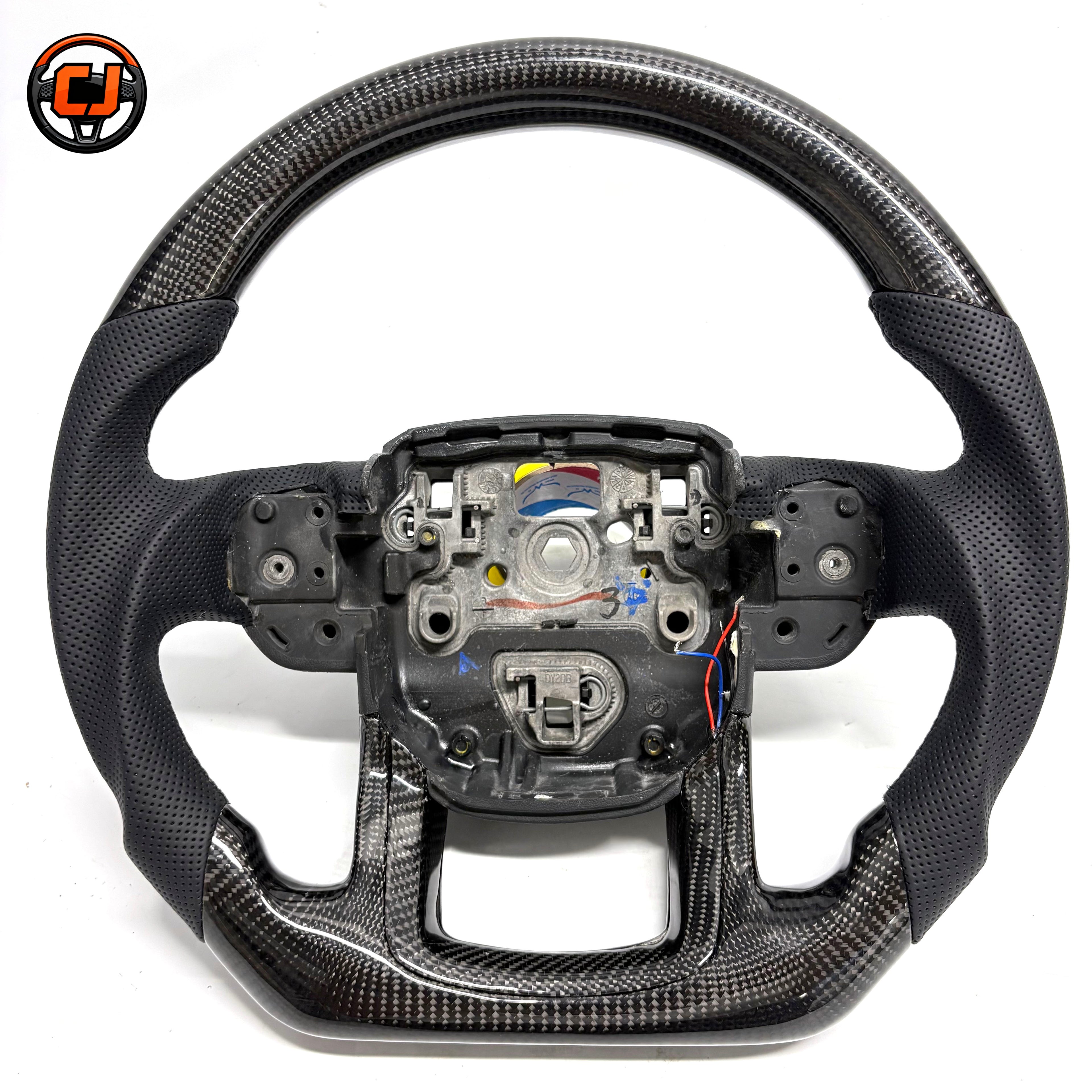 Studio product photo of custom Range Rover Evoque carbon fiber steering wheel with black perforated leather grips, flat bottom carbon fiber trim and exposed central mounting structure