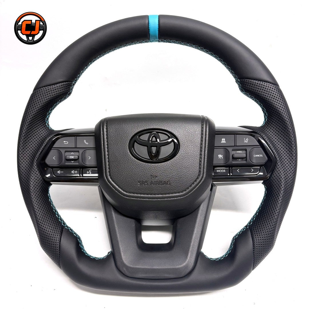 Toyota Land Cruiser LC300 handcrafted leather steering wheel with perforated grip sections, blue contrast stitching, OEM airbag cover and factory-style controls by CJ Mod Garage