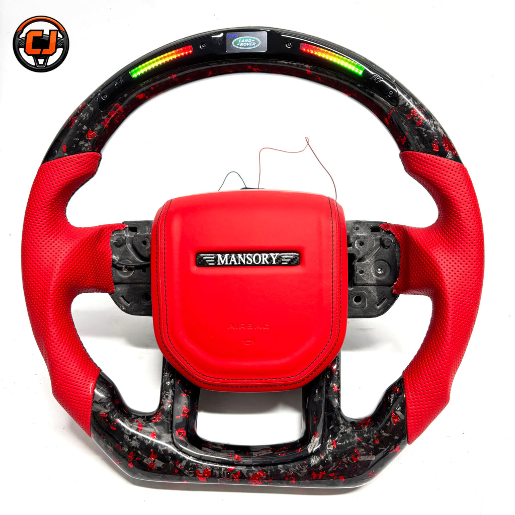 Studio product photo of custom Land Rover Range Rover steering wheel with red leather airbag cover, red perforated leather grips, LED shift lights and red black forged carbon fiber trim