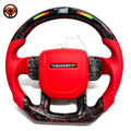 Studio product photo of custom Land Rover Range Rover steering wheel with red leather airbag cover, red perforated leather grips, LED shift lights and red black forged carbon fiber trim