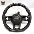 Studio product photo of custom Jeep Wrangler carbon fiber steering wheel with LED shift lights, top digital display, black perforated leather grips, flat bottom design and exposed button openings