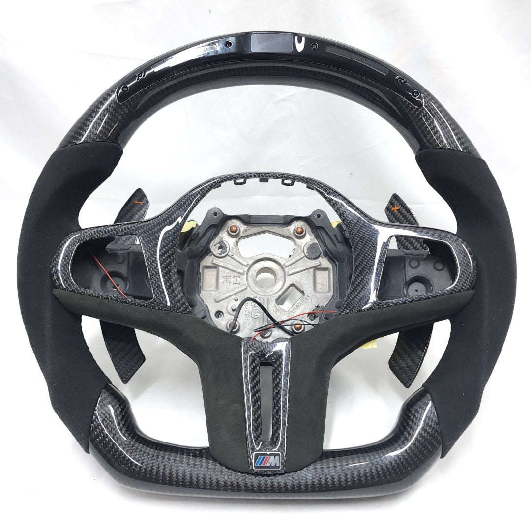 BMW G-chassis carbon fiber LED steering wheel frame on white background with Alcantara side grips, carbon paddle shifters, integrated LED display, and flat-bottom motorsport styling for BMW G02 G05 G06 G09 G11 G12 G15 G20 G22 G28 G29 G30 G38 G80 G82 F40 F90 by CJ Mod Garage