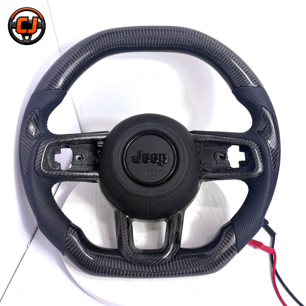 Front studio product image of custom Jeep Wrangler carbon fiber steering wheel with black perforated leather side grips, glossy carbon fiber upper and lower sections, black airbag cover and OEM style button openings