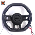 Front studio product image of custom Jeep Wrangler carbon fiber steering wheel with black perforated leather side grips, glossy carbon fiber upper and lower sections, black airbag cover and OEM style button openings