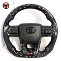 Custom Toyota Land Cruiser steering wheel with black forged carbon composite and white flake accents, OEM airbag cover and multifunction buttons by CJ Mod Garage