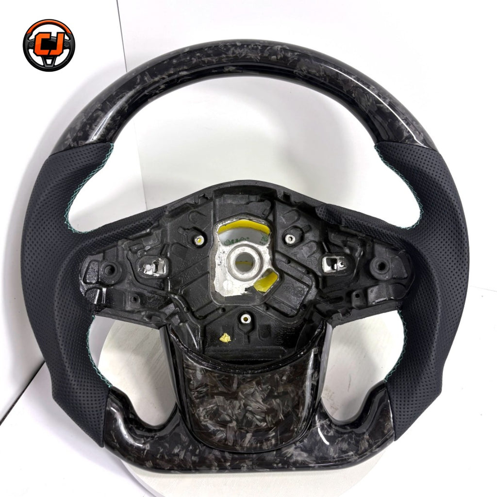 Toyota Supra A90 performance steering wheel in forged carbon composite with perforated leather side grips and handcrafted turquoise stitching by CJ Mod Garage