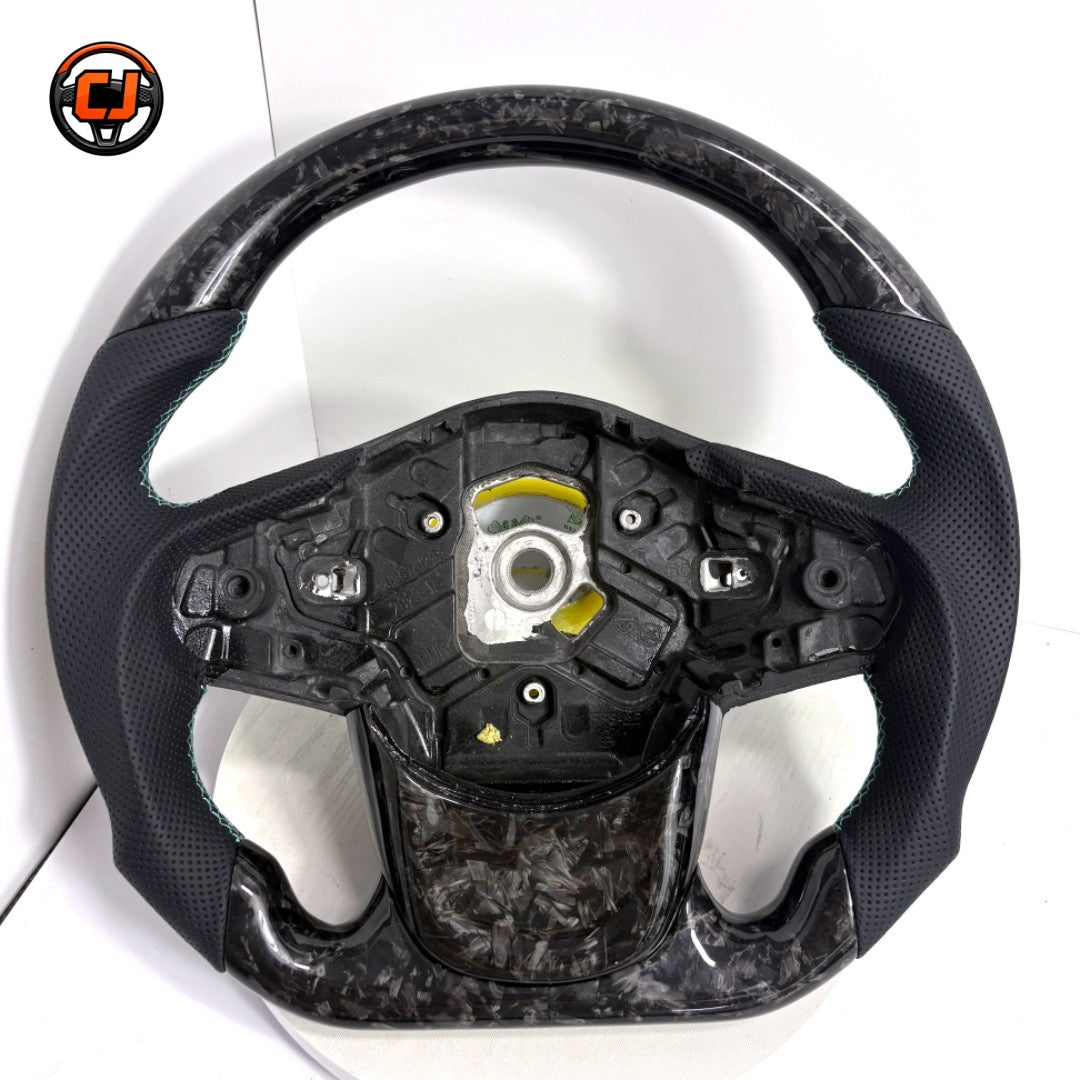 Toyota Supra A90 performance steering wheel in forged carbon composite with perforated leather side grips and handcrafted turquoise stitching by CJ Mod Garage