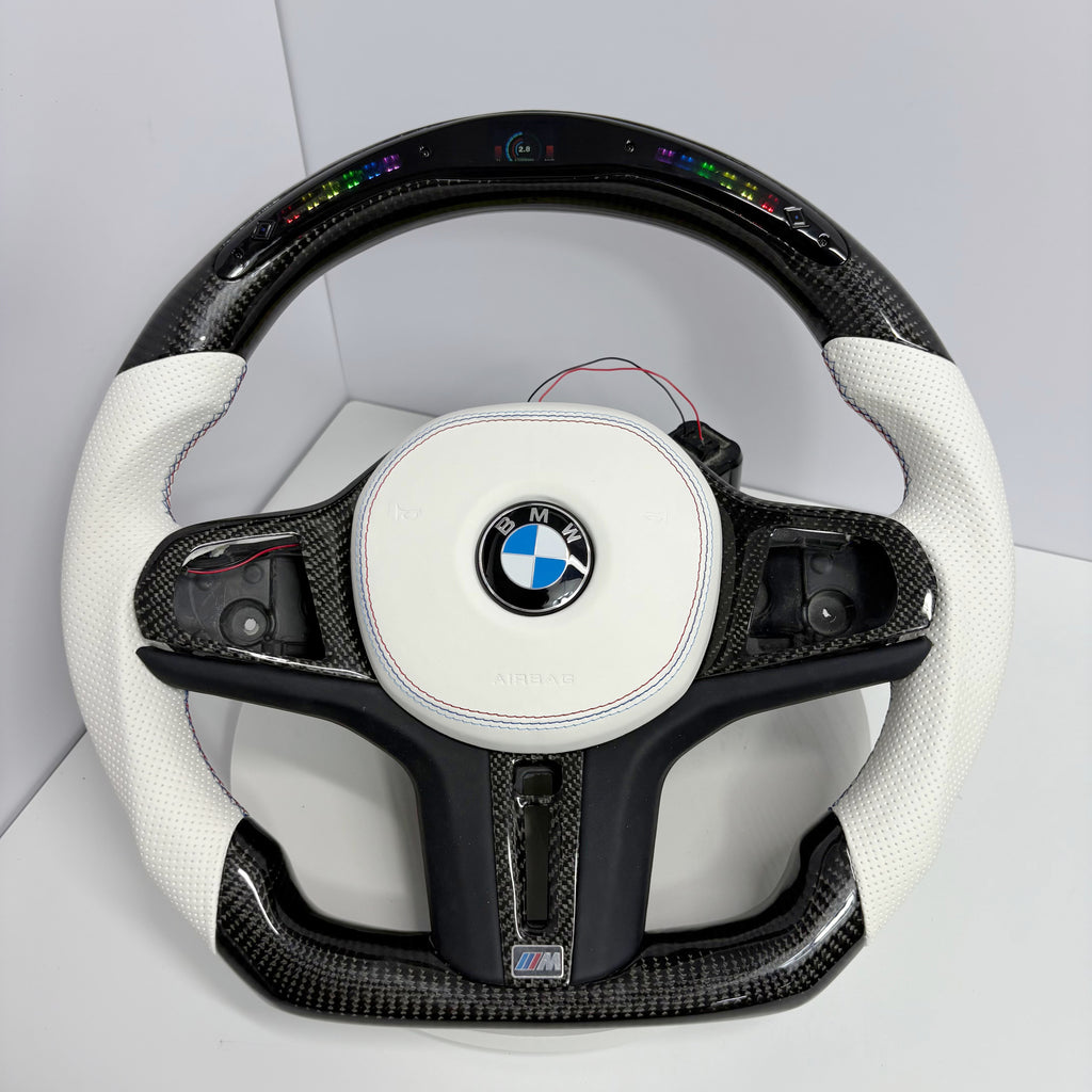 BMW custom LED carbon fiber steering wheel by CJ Mod Garage on white background featuring gloss carbon fiber top and bottom, white perforated leather side grips, integrated LED shift light display, white round airbag cover, flat-bottom M Performance design, and fitment for BMW G02 G05 G06 G09 G11 G12 G15 G20 G22 G28 G29 G30 G38 G80 G82 F40 F90