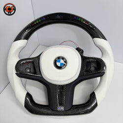 BMW custom LED carbon fiber steering wheel by CJ Mod Garage on white background featuring gloss carbon fiber top and bottom, white perforated leather side grips, integrated LED shift light display, white round airbag cover, flat-bottom M Performance design, and fitment for BMW G02 G05 G06 G09 G11 G12 G15 G20 G22 G28 G29 G30 G38 G80 G82 F40 F90