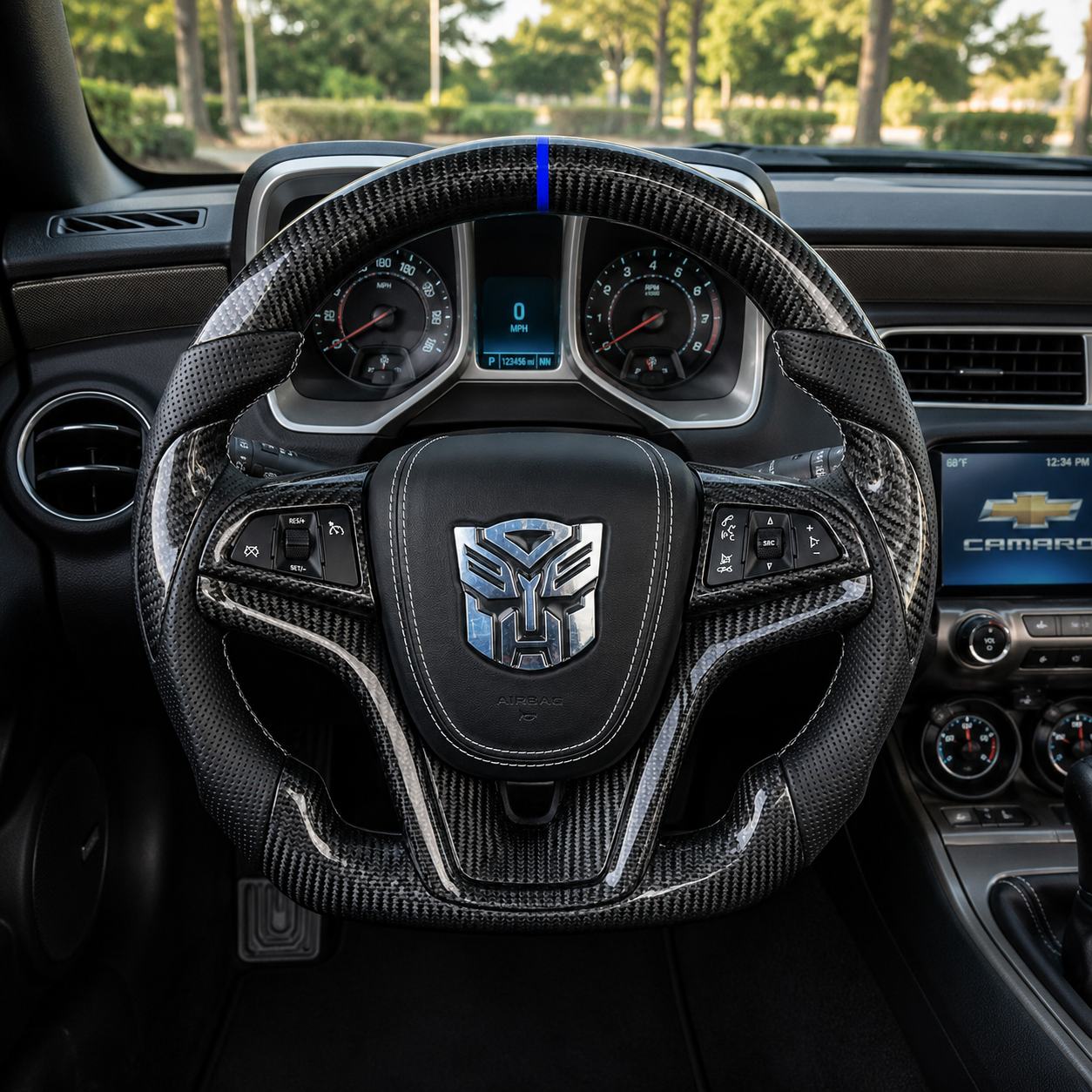 Front interior view of custom Chevrolet Camaro steering wheel with gloss carbon fiber finish blue center stripe black perforated grips white stitching and silver transformer emblem