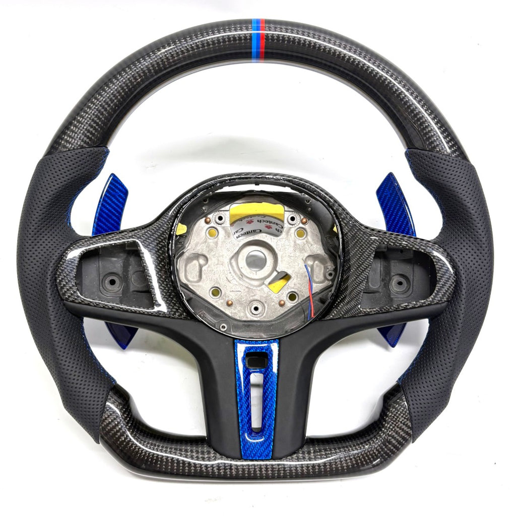 CJ Mod Garage BMW G-chassis custom carbon fiber steering wheel on white background featuring gloss carbon fiber top and bottom, black perforated leather grips, blue forged carbon center trim and paddle shifters, flat-bottom OEM+ sport design, compatible with BMW G02 G05 G06 G09 G11 G12 G15 G20 G22 G28 G29 G30 G38 G80 G82 F40 F90