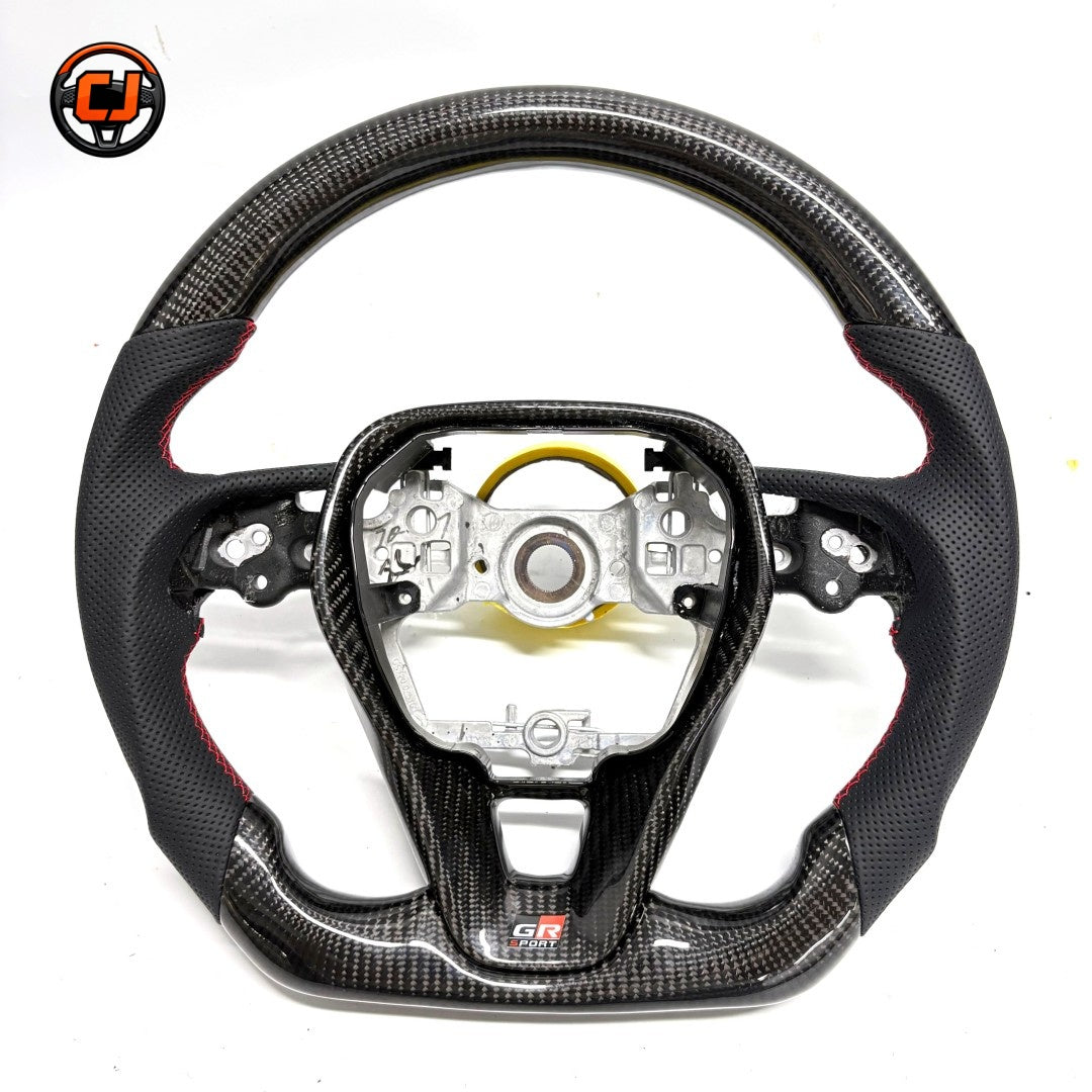 Toyota GR Corolla carbon fiber flat-bottom steering wheel frame with premium perforated leather grip areas and OEM-style fitment by CJ Mod Garage