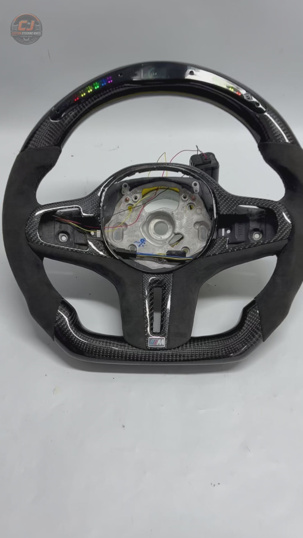 White background showcase video of CJ Mod Garage BMW LED carbon fiber steering wheel featuring RGB LED shift light system, integrated digital RPM display, gloss carbon fiber finish, Alcantara performance grips, flat-bottom motorsport styling, OEM-inspired fitment and compatibility with BMW G02 G05 G06 G09 G11 G12 G15 G20 G22 G28 G29 G30 G38 G80 G82 F40 F90 models
