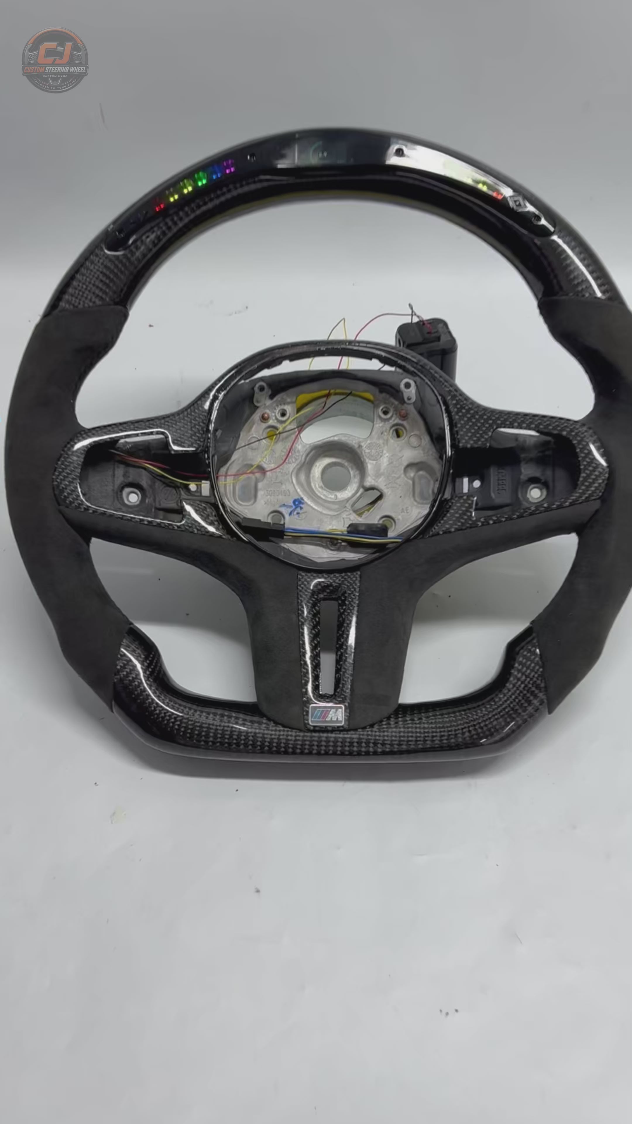 White background showcase video of CJ Mod Garage BMW LED carbon fiber steering wheel featuring RGB LED shift light system, integrated digital RPM display, gloss carbon fiber finish, Alcantara performance grips, flat-bottom motorsport styling, OEM-inspired fitment and compatibility with BMW G02 G05 G06 G09 G11 G12 G15 G20 G22 G28 G29 G30 G38 G80 G82 F40 F90 models
