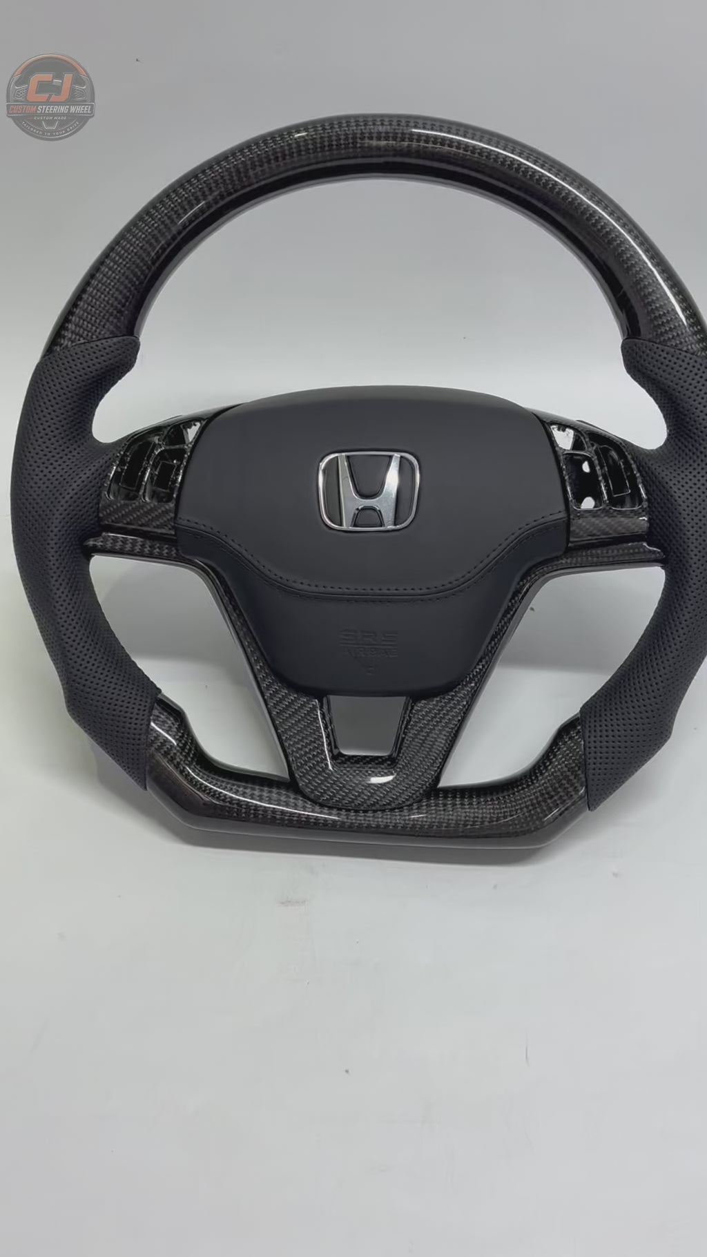 Honda CR-V 2007-2011 carbon fiber steering wheel rotating on white background with perforated leather grips OEM airbag cover and factory fitment by CJ Mod Garage