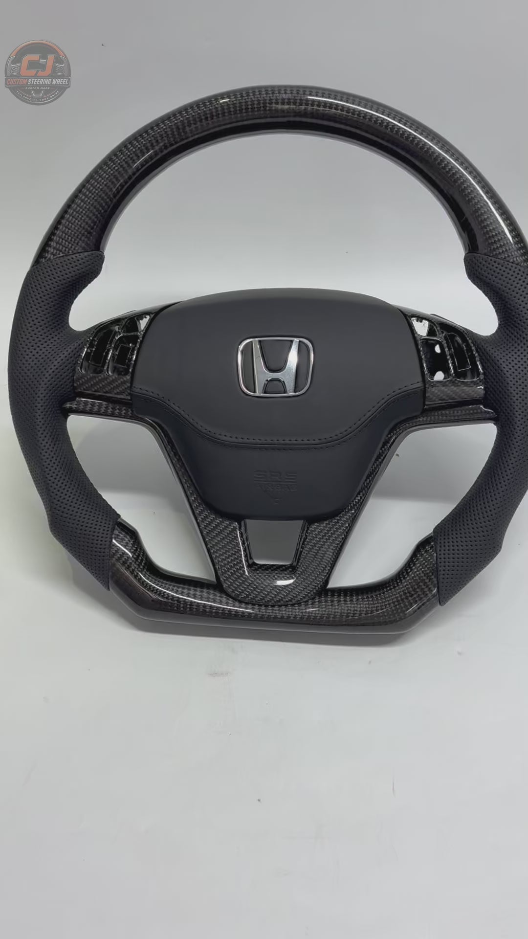 Honda CR-V 2007-2011 carbon fiber steering wheel rotating on white background with perforated leather grips OEM airbag cover and factory fitment by CJ Mod Garage