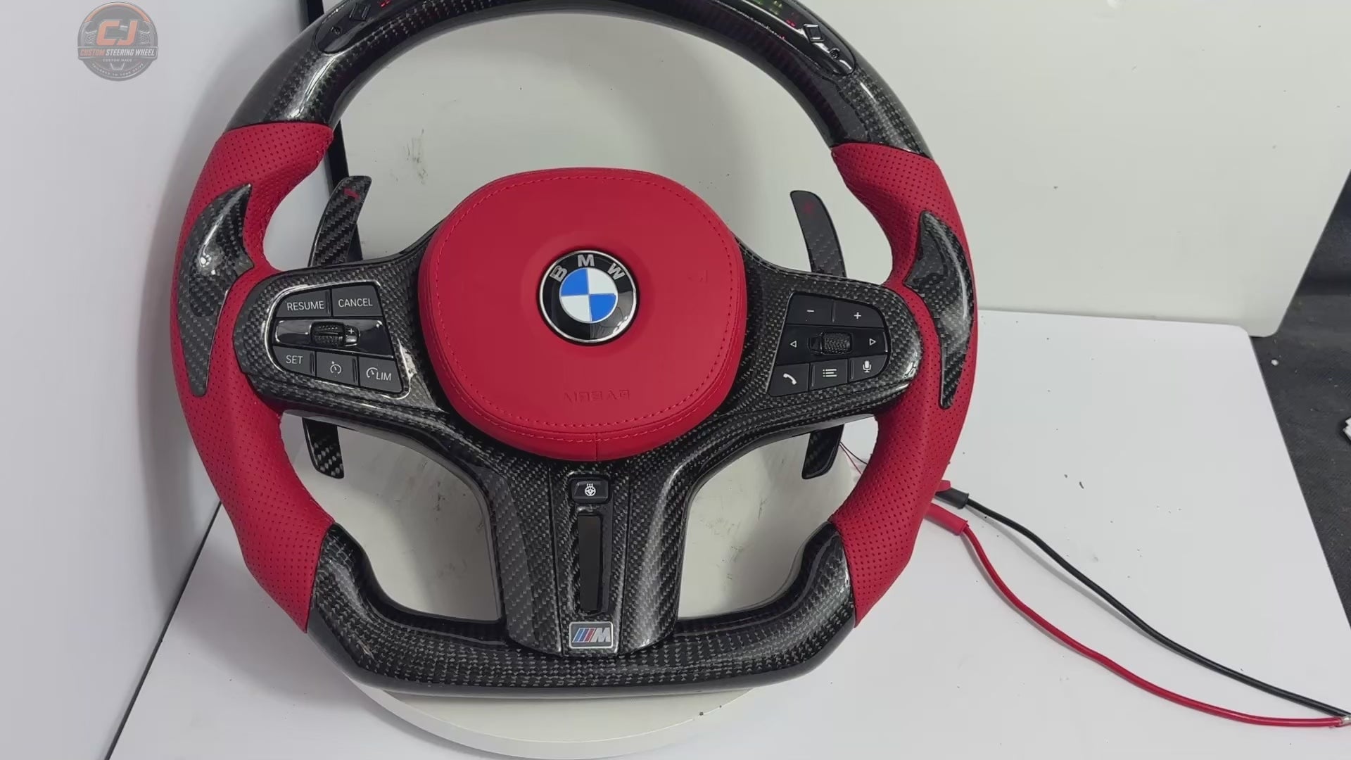 White background product video of a BMW custom carbon fiber steering wheel featuring LED shift lights, digital display, red perforated leather grips and flat-bottom M performance styling for BMW G02 G05 G06 G09 G11 G12 G15 G20 G22 G28 G29 G30 G38 G80 G82 F40 F90 – CJ Mod Garage