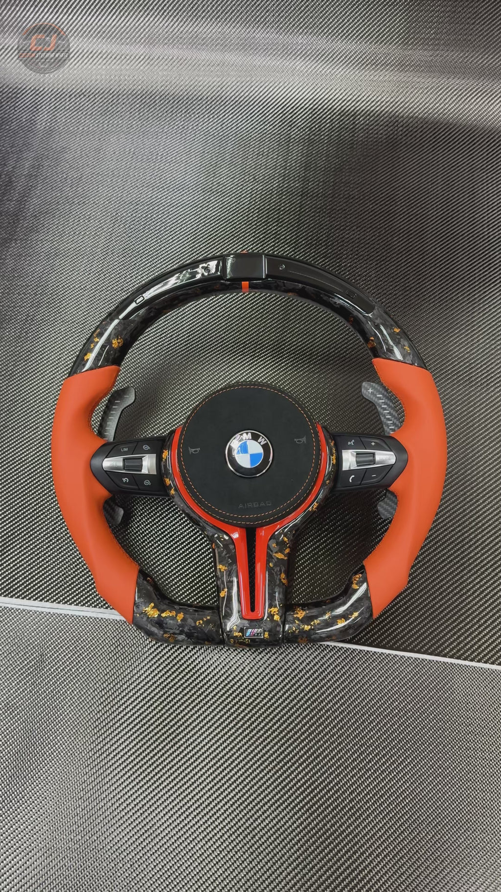 360-degree white background product video of custom BMW forged carbon fiber steering wheel with gold flakes, orange leather grips, RGB LED shift indicator display, multifunction buttons, and carbon paddle shifters for BMW F10 F11 F15 F18 F20 F23 F25 F30 F32 F35 F40 F80 E84 E87 E90 E92 E93