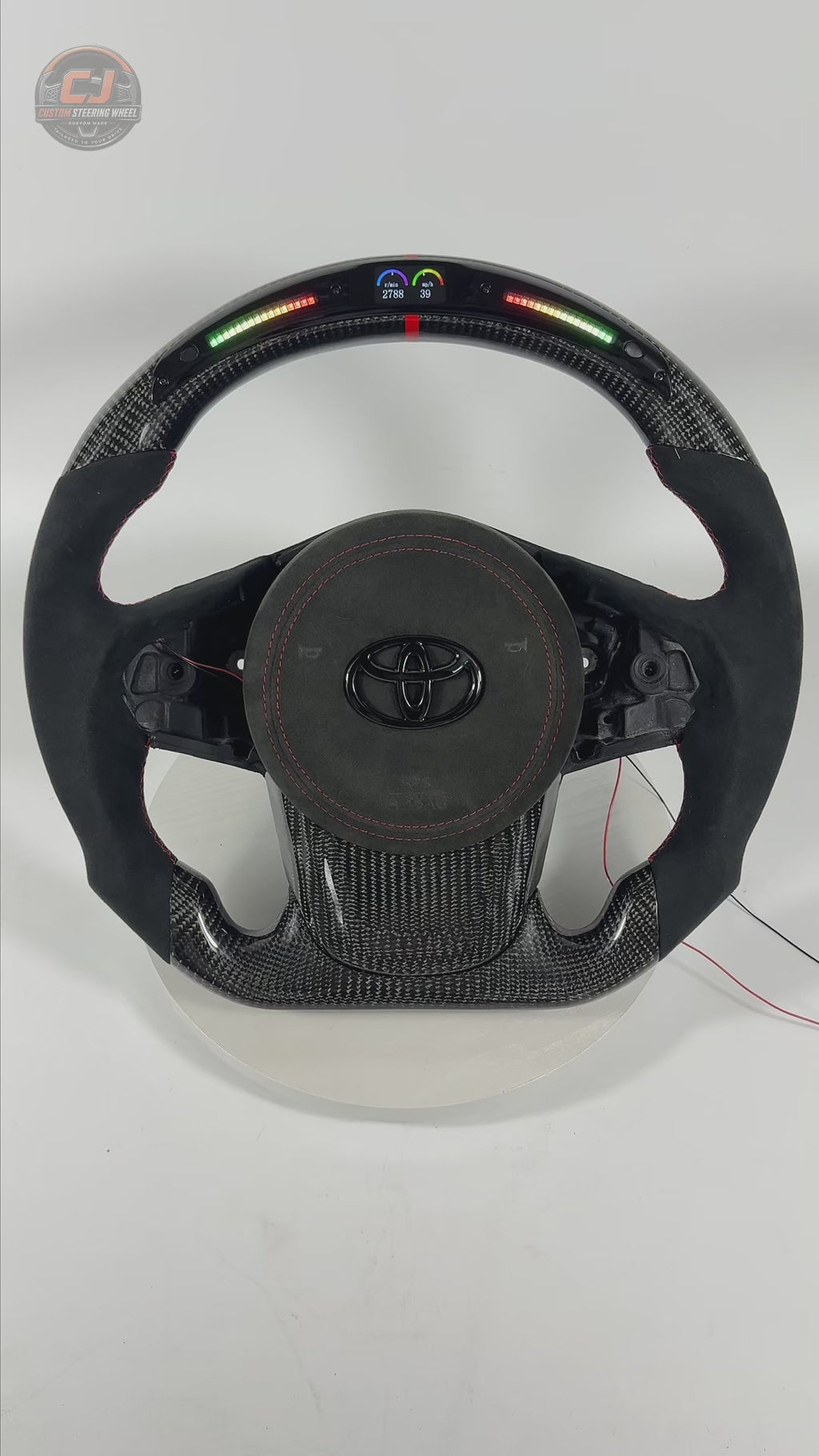 Product showcase video of Toyota Supra A90 A91 carbon fiber steering wheel with LED shift light display, Alcantara grip material, red stitching details and custom racing design by CJ Mod Garage
