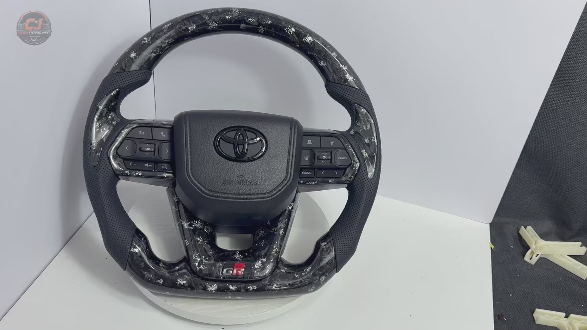 360-degree product video of Toyota LC300 forged carbon steering wheel with white flake finish, perforated leather grips, OEM button layout and plug-and-play fitment by CJ Mod Garage