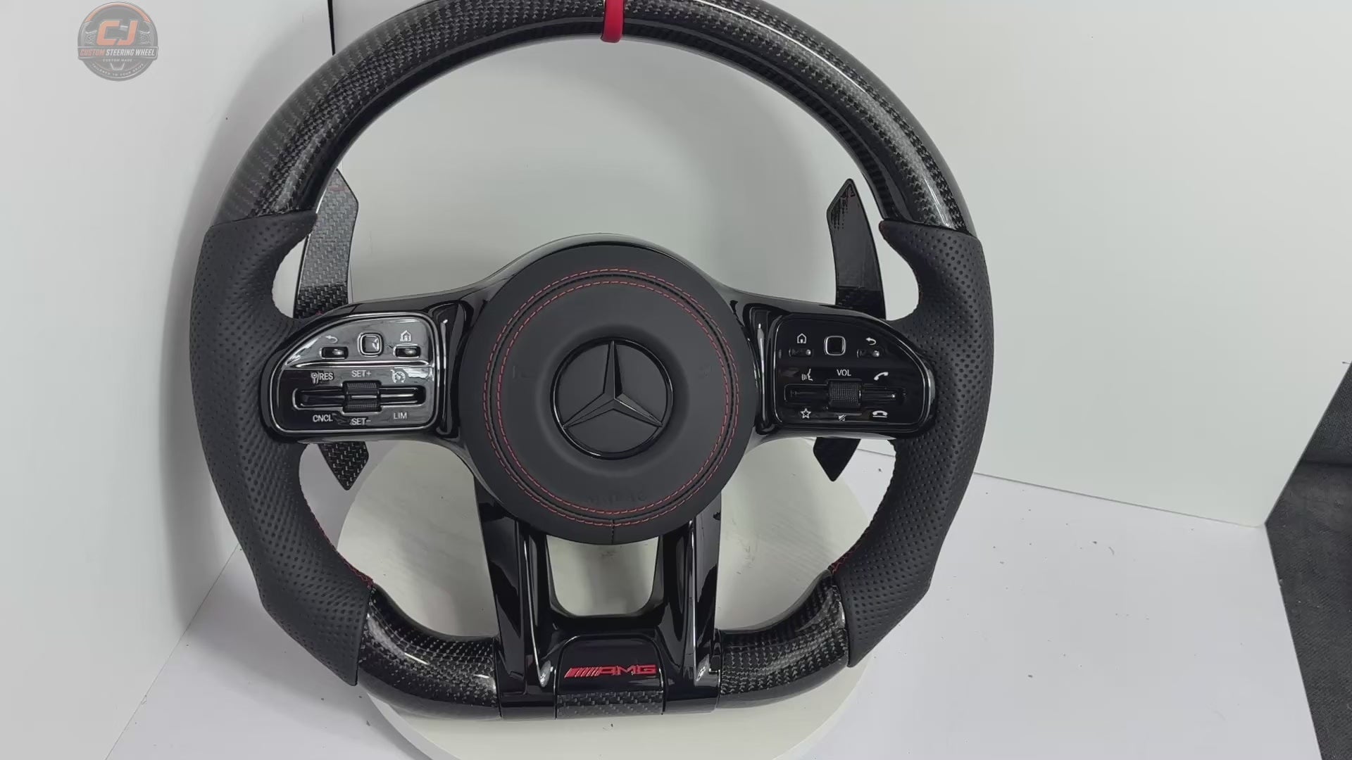 White background video showing Mercedes AMG carbon fiber steering wheel with red twelve clock stripe perforated leather grips paddle shifters and sporty airbag cover for W117 W176 W177 W203 W204 W205 W211 W212 W213 W218 C43 C63 C200 C300 CJ Mod Garage