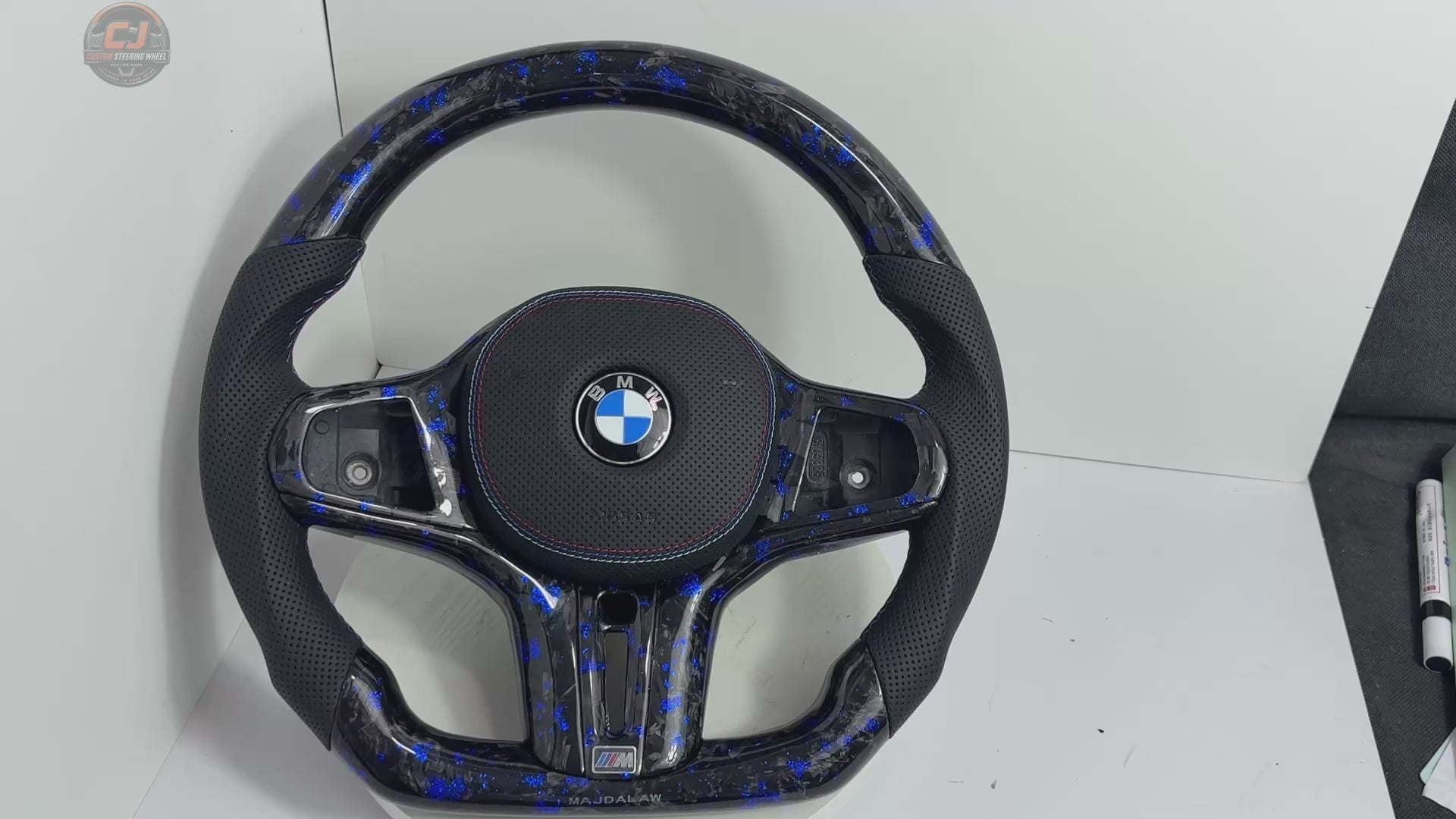 360-degree white background product video showcasing a custom BMW forged carbon fiber steering wheel with electric-blue flakes, perforated leather grips, flat-bottom M-style shape and premium handcrafted finish. Video highlights glossy forged carbon texture, ergonomic grip design, detailed stitching and sporty performance styling for BMW G02 G05 G06 G09 G11 G12 G15 G20 G22 G28 G29 G30 G38 G80 G82 F40 F90 models – CJ Mod Garage