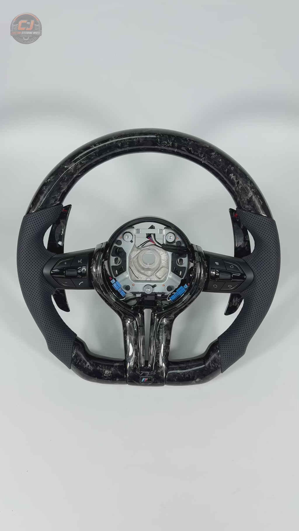 360-degree white background product video of custom BMW forged carbon fiber steering wheel with black perforated leather grips, multifunction buttons, paddle shifters, and OEM fitment for BMW F10 F11 F15 F18 F20 F23 F25 F30 F32 F35 F40 F80 E84 E87 E90 E92 E93