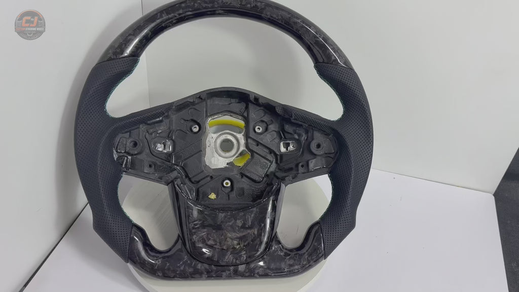 Rotating studio video of Toyota GR Supra A90 A91 forged carbon steering wheel showcasing gray flake carbon fiber, perforated leather grips, flat-bottom design and custom detailing by CJ Mod Garage