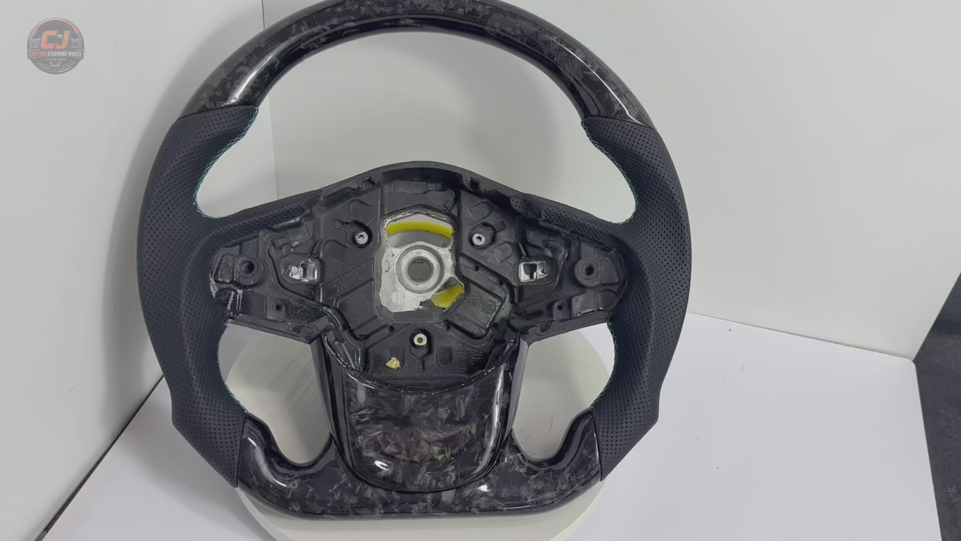 Rotating studio video of Toyota GR Supra A90 A91 forged carbon steering wheel showcasing gray flake carbon fiber, perforated leather grips, flat-bottom design and custom detailing by CJ Mod Garage