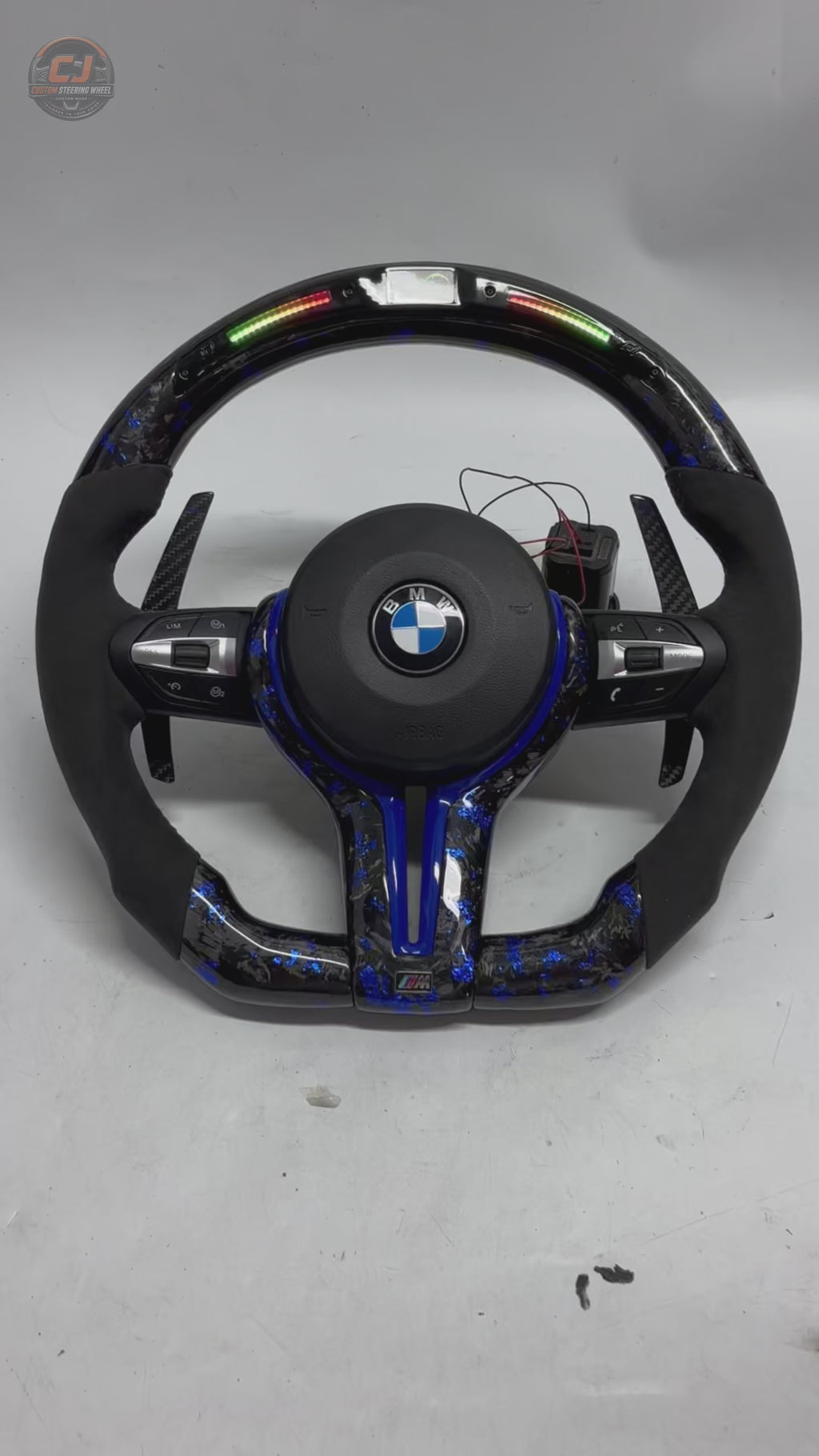 360-degree white background video of BMW F Series and E Series custom forged carbon fiber steering wheel featuring blue forged carbon accents, LED shift lights, Alcantara grips, multifunction controls, and carbon paddle shifters