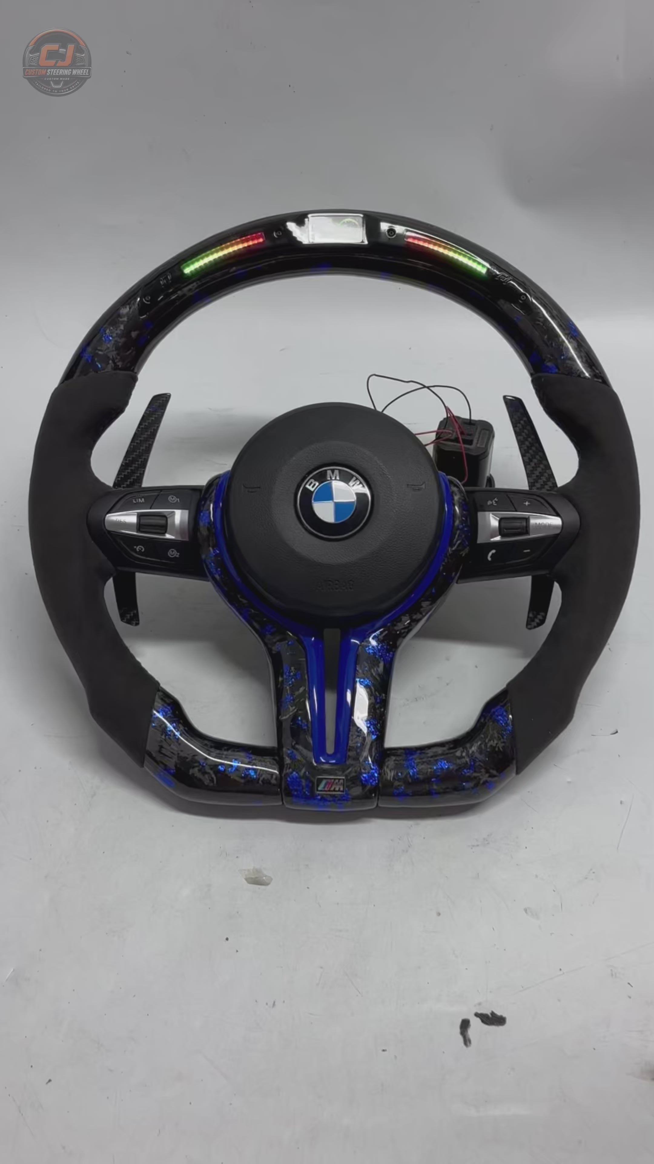 360-degree white background video of BMW F Series and E Series custom forged carbon fiber steering wheel featuring blue forged carbon accents, LED shift lights, Alcantara grips, multifunction controls, and carbon paddle shifters