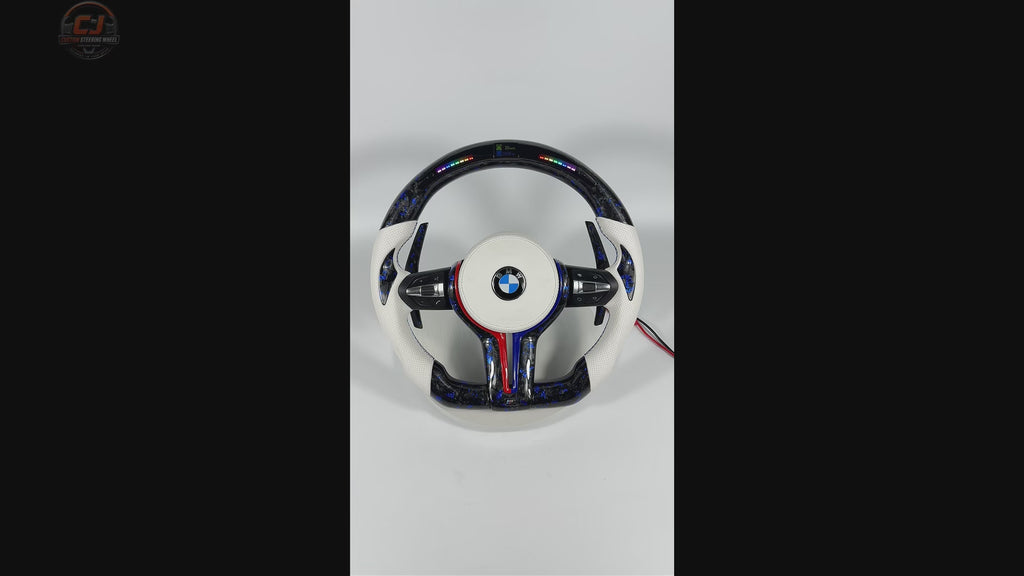 360-degree white background video of custom BMW forged carbon fiber steering wheel with blue flakes, LED shift indicator display, white perforated leather grips, multifunction controls, and carbon paddle shifters for BMW F10 F11 F15 F18 F20 F23 F25 F30 F32 F35 F40 F80 E84 E87 E90 E92 E93