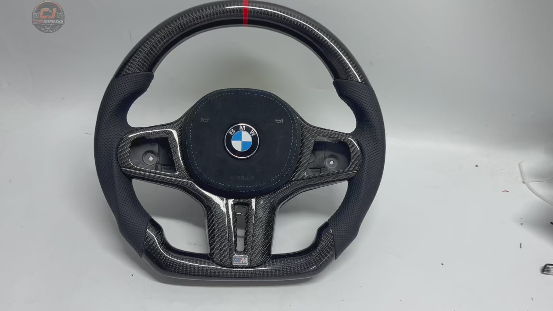 White background showcase video of custom BMW G-series carbon fiber steering wheel with perforated leather grips, blue stitching, flat-bottom OEM+ performance design, and red center stripe compatible with BMW G02 G05 G06 G09 G11 G12 G15 G20 G22 G28 G29 G30 G38 G80 G82 F40 F90