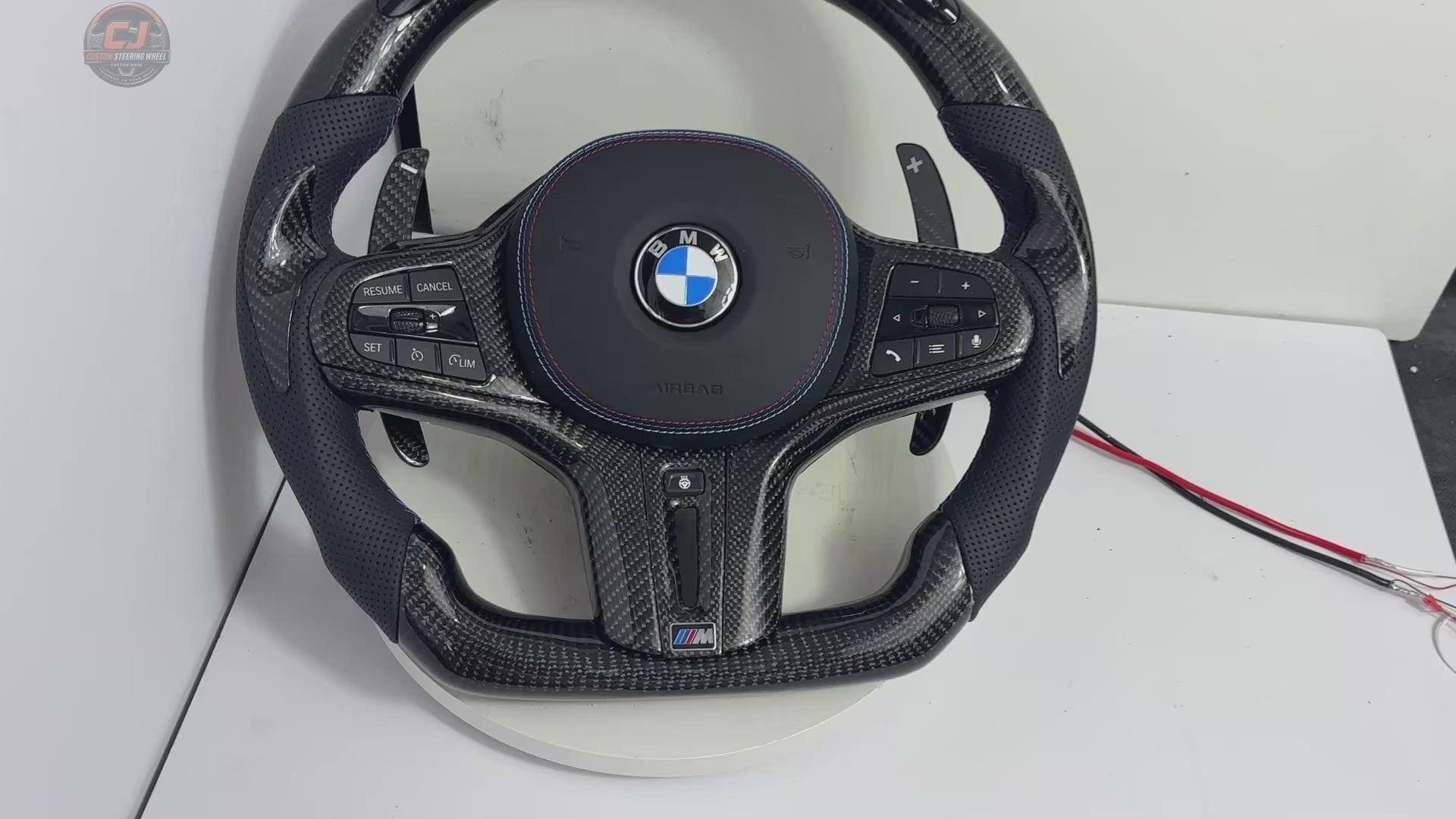 White studio video showing a BMW custom carbon fiber steering wheel with LED shift indicator, digital display, perforated leather grips and carbon paddles for BMW G02 G05 G06 G09 G11 G12 G15 G20 G22 G28 G29 G30 G38 G80 G82 F40 F90 by CJ Mod Garage