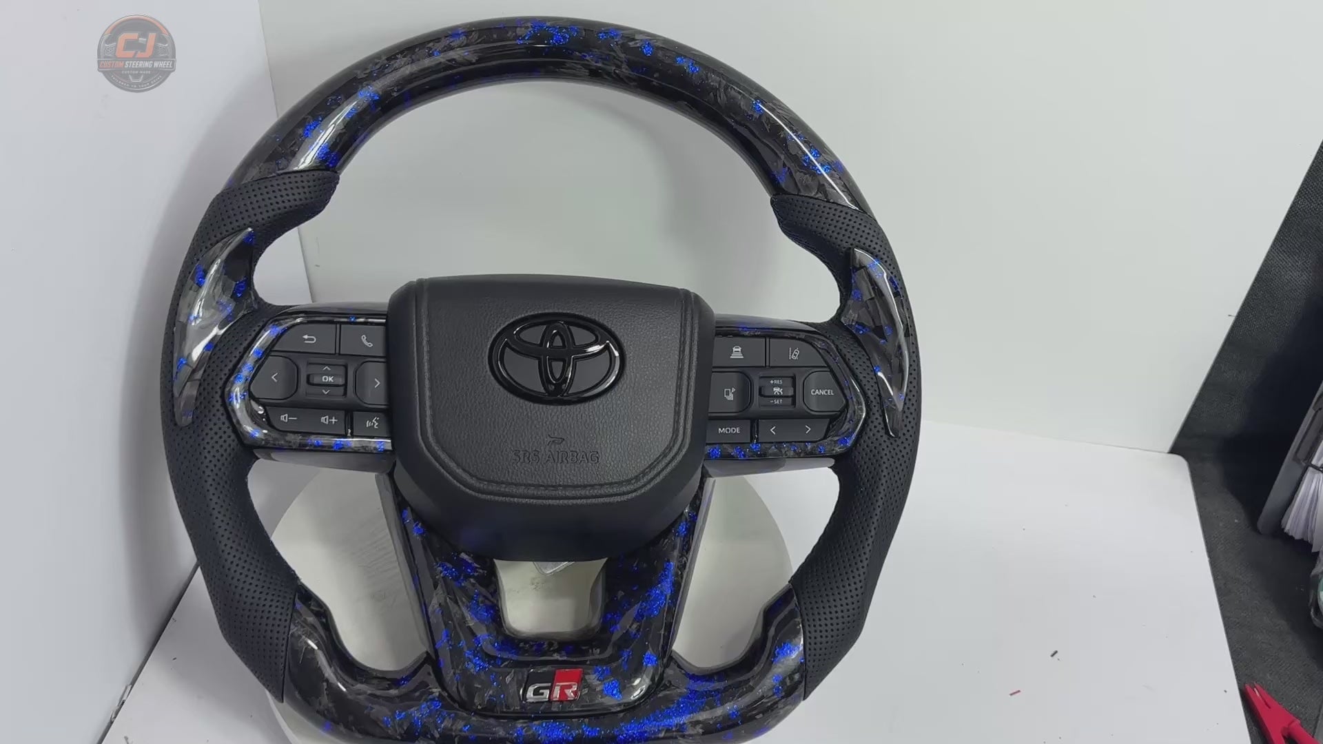 White background showcase video of Toyota LC300 Prado Hilux Land Cruiser steering wheel with blue forged carbon style material perforated leather grips GR sport styling and custom craftsmanship by CJ Mod Garage